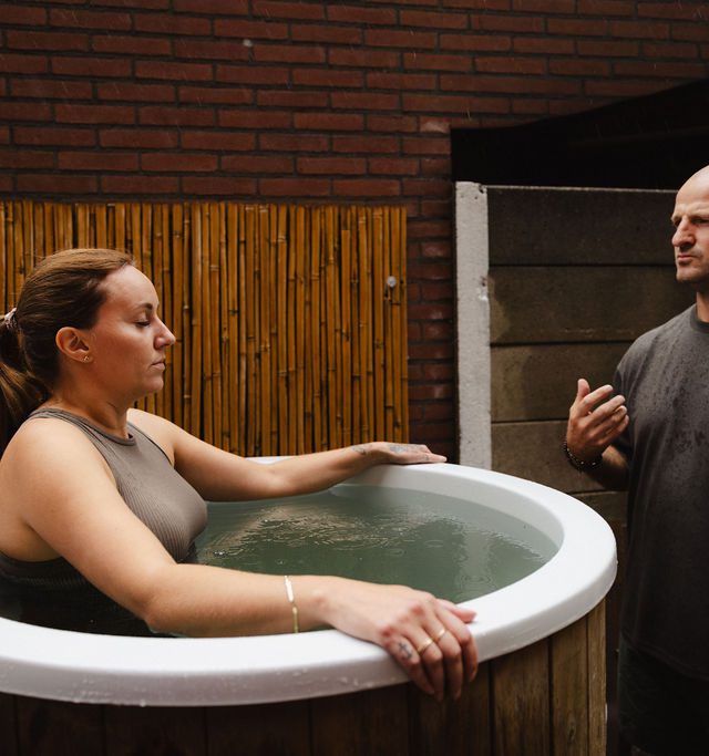 Deelnemer in het ijsbad met begeleiding van een coach